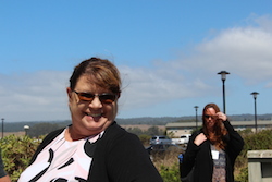 Woman in foreground smiles at camera, woman in background brushes hair out of her face